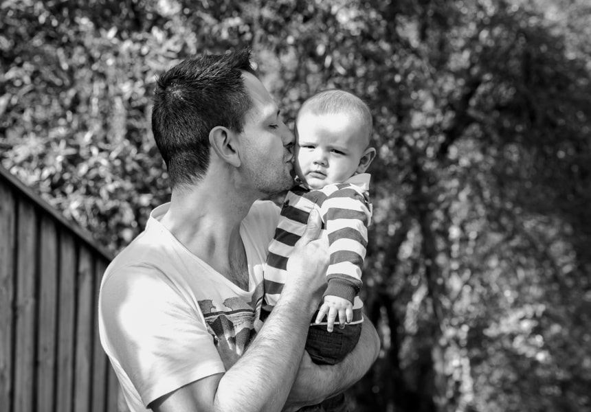 Black and White photo of Lennox Hastie holding his son in his arms and kissing him on his cheeks.